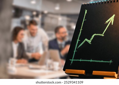 This image features a chalkboard displaying a graph with an upward trend, symbolizing growth or success, with a group of blurred business professionals in the background. - Powered by Shutterstock