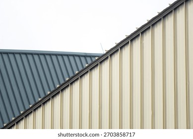 This image features a close view of two distinct roofs made from metallic panels, showcasing angles, textures, and a modern architectural design against a cloudy sky.