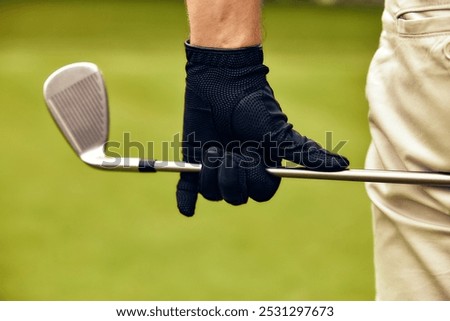 This image features a closeup of a golfer gripping an iron club, showcasing a black glove that contrasts beautifully with the vibrant green background, creating a visually stunning scene