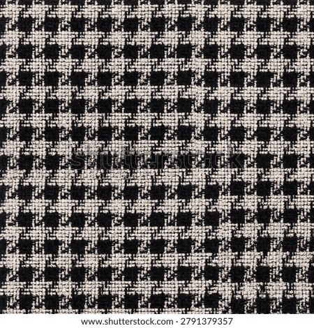 This image features a close-up, top-down view of a classic houndstooth textile pattern. The fabric displays a tightly woven, repeating geometric motif characterized by broken checks or abstract four-pointed shapes. It utilizes a high-contrast color scheme consisting of deep black and off-white or cream-colored threads. The texture appears dense, tactile, and heavily textured, characteristic of heavy wool, tweed, or upholstery-grade woven material. The interlacing of the yarns creates a distinct grid-like structural appearance under close inspection. This timeless pattern is commonly found in traditional tailored apparel, outerwear, and interior design textiles.