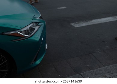 This image features a closeup view of a vibrant teal car parked neatly on a bustling city street, highlighting its front end and the dynamic surroundings in the urban environment