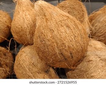 This image features a close-up view of several whole coconuts with their fibrous husks still intact. The brown coconuts covered in coarse, stringy fibers, giving them a rugged, natural appearance 