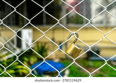 This image features a close-up view of a brass padlock attached to a metal chain-link fence, symbolizing security, protection, and boundary demarcation in outdoor settings.