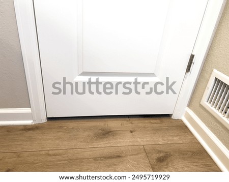 This image features a close-up view of a section of newly installed wood flooring, highlighting the area at the base of a white door. The wood flooring has a light, natural finish with visible wood