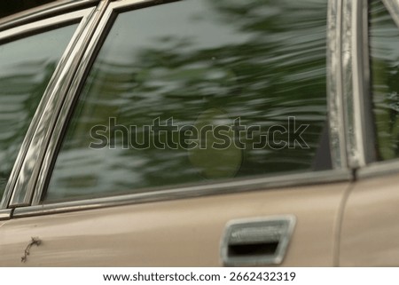 This image features a closeup view of a car window, showcasing a beautiful reflection of trees and greenery in the glass surface