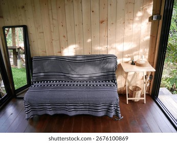 This image features a cozy interior with a black and white striped sofa set against a natural wooden wall. Ideal for showcasing minimalist decor and tranquility.