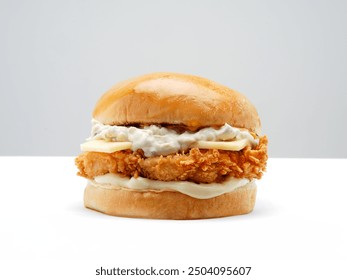 This image features a crispy chicken sandwich with a glossy brioche bun, white cheddar cheese topped with a special sauce, and mayonnaise, all set against a clean, white background.







