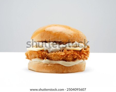 This image features a crispy chicken sandwich with a glossy brioche bun, white cheddar cheese topped with a special sauce, and mayonnaise, all set against a clean, white background.






