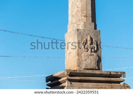 This image features a detailed stone carving of a Jain Tirthankara on an ancient pillar in the historic town of Shravanabelagola, set against a serene blue sky.