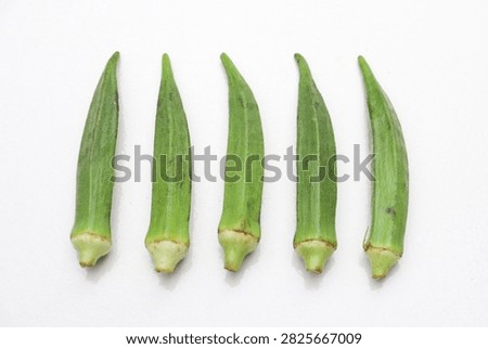 This image features five freshly picked, vibrant green okra pods aligned in a row against a pristine white background, highlighting their natural texture and color.