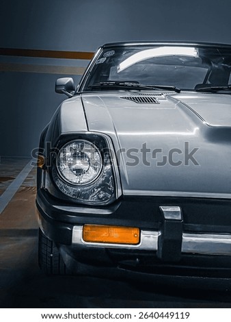 This image features the front of a classic car, with a prominent circular headlight, parked indoors.