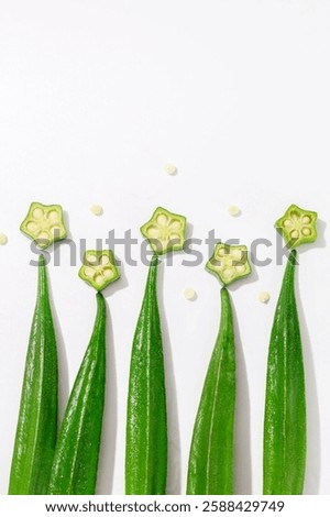 This image features a green okra vegetable placed on a white surface. The contrast between the vibrant green color of the vegetable and the neutral white background highlights its freshness. 