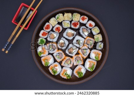 This image features a large circular wooden platter filled with an array of sushi rolls, perfectly arranged in a circular pattern. The assortment includes a selection of rolls with fresh fish, avocado
