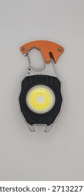 This image features a multi-functional keychain flashlight, equipped with a carabiner clip, showcasing an orange handle and a bottle opener located at the bottom.