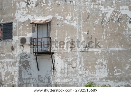 This image features an old, weathered building exterior with peeling paint, a small rusted metal balcony, and a window, showcasing vintage urban architecture and environmental decay.
