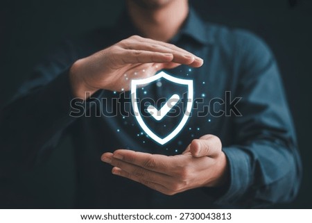 This image features a person's hands cupped around a vibrant, glowing digital shield icon that contains a clear checkmark. The blue light emanates from the shield, signifying robust security and protection. It's a powerful visual for concepts related to cybersecurity, data protection, insurance, quality assurance, safety, and overall reliability in digital and real-world contexts.