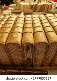 This image features rows of old leather-bound books with gold embossing on their spines. The books are arranged on a bookshelf, showcasing their ornate details and classic design. 