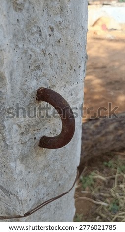 This image features a rusted metal U-bolt or hook embedded securely into a weathered, light-colored concrete post, likely used for heavy-duty anchoring.