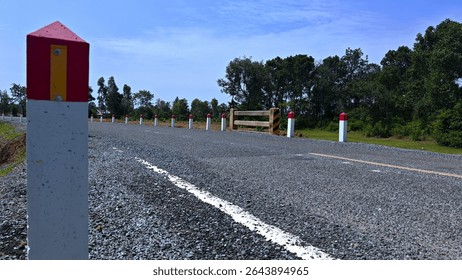 This image features a scenic empty road lined with pylon markers under a bright blue sky, surrounded by lush greenery, creating a serene landscape perfect for travel themes.