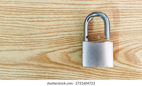 This image features a silver padlock placed on a wooden surface with prominent grain patterns. The padlock is a common symbol of security, safety, and protection. The wooden background adds a natural element to the scene, contrasting with the metallic padlock. The image could be used to represent themes of security, protection, and safety in various contexts.