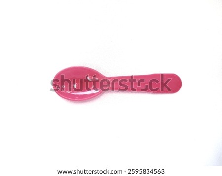 This image features a small pink plastic spoon. The spoon has a rounded, curved shape and appears to be designed for desserts or small servings.