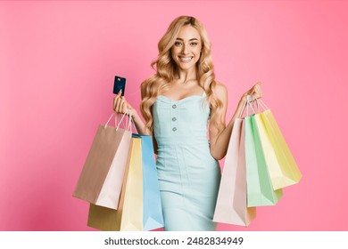 This image features a smiling young woman with long blonde hair, wearing a light blue dress, holding a stack of brightly colored shopping bags and a credit card in her hands against pink
