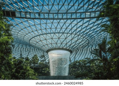 This image features a stunning indoor waterfall surrounded by lush tropical plants inside a large glass dome, showcasing architectural innovation and natural beauty. - Powered by Shutterstock