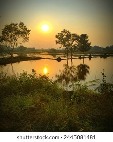 This image features a tranquil landscape of a body of water with trees and a sunset in the background. The scene captures the natural beauty of the outdoor setting with its calm water