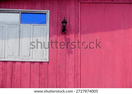 This image features a vibrant pink exterior wall accentuated by a white window and a vintage lantern, creating a charming and inviting atmosphere.