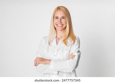 This image features a woman with blonde hair wearing a white lab coat, smiling at the camera with her arms crossed. The background is a plain white wall. - Powered by Shutterstock