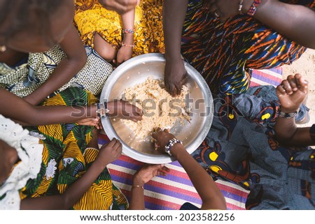 In this image, a group of African girls is sitting in a circle around a large plate of cereals, eating their meager vegan meal together with their hands