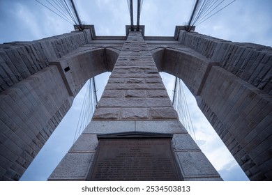 This image offers a dramatic upward view of the Brooklyn Bridge's iconic stone towers and suspension cables.  - Powered by Shutterstock