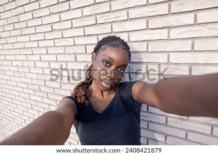 This image offers a fresh perspective on the ubiquitous selfie, with a young Black woman as the protagonist. Her arm outstretched to capture the perfect shot, she gives the camera a direct, engaging