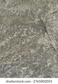 This image presents a macro view of a rough-hewn stone surface, likely granite or a similar igneous rock. The texture is highly irregular and granular, featuring a mix of charcoal, ash, and light grey tones. Small mineral flecks catch the light, creating a subtle sparkle against the otherwise matte, weathered finish. Its rugged and durable appearance makes it a classic element in architectural cladding, outdoor monuments, or natural landscape features.