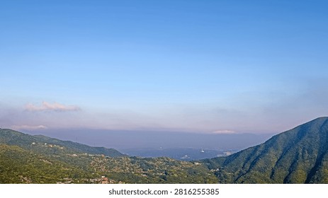 This image presents a stunning panoramic view from Teapot Mountain in Taiwan, looking toward the Pacific Ocean. The high-angle perspective captures layered mountain ridges sloping down to the coastline, where the sea meets a hazy sky. Bright sunlight reflects beautifully off the water, highlighting the majestic landscape.
