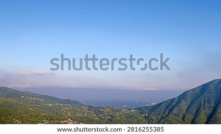 This image presents a stunning panoramic view from Teapot Mountain in Taiwan, looking toward the Pacific Ocean. The high-angle perspective captures layered mountain ridges sloping down to the coastline, where the sea meets a hazy sky. Bright sunlight reflects beautifully off the water, highlighting the majestic landscape.