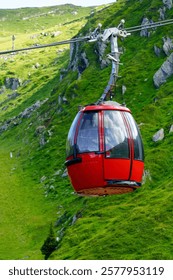 This is an image of a red and modern cable car going up the mountainside. The cable car is surrounded by lush green trees and a beautiful mountain landscape.