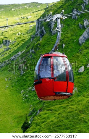 This is an image of a red and modern cable car going up the mountainside. The cable car is surrounded by lush green trees and a beautiful mountain landscape.
