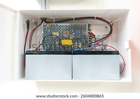 This image showcases an electrical power supply system featuring two batteries within a wall-mounted enclosure, highlighting essential wiring and connections.