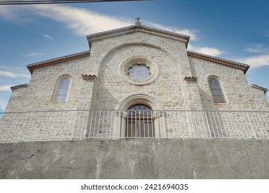 This image showcases the front facade of a serene stone church located in the picturesque Ardeche region. The church, constructed with traditional stonemasonry, presents a robust and time-honored