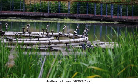 This image showcases a functional aeration and fountain system, an essential component of urban water management, submerged within a public park pond. The intricate network of textured pipes and nozzles, reflecting industrial design, creates a geometric composition amidst the aquatic scenery