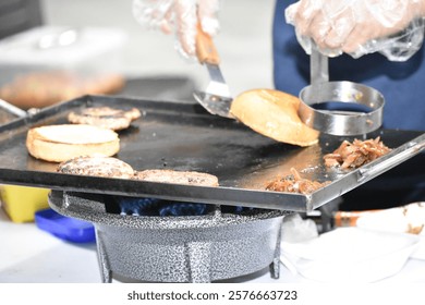 This image showcases the process of making burgers at a street food stall in Malaysia, reflecting the vibrant street food culture popular among locals. Burgers are being cooked on a large flat griddle