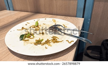 This image shows an almost empty white plate with leftover fried noodles, scattered crumbs, and a fork and spoon, indicating a recently finished meal.