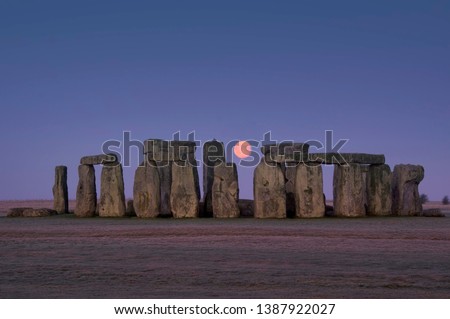 This image shows the ancient stones of Stonehenge with glowing moon between megaliths, Wiltshire, England
