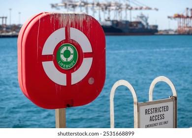 This image shows a bright red lifebuoy station situated by the waterfront.  - Powered by Shutterstock