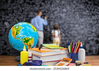 This image shows a classroom scene where various educational tools, such as a globe, books, notebooks, colored pencils, and a calculator, are placed on a desk in the foreground. In the background. - Powered by Shutterstock