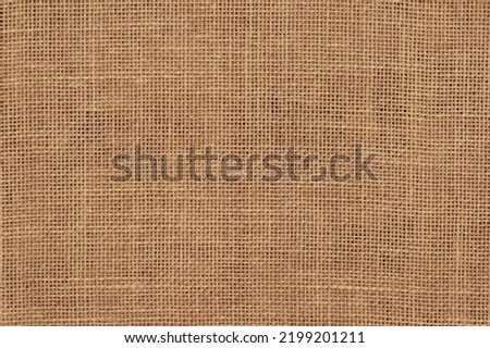 This image shows a close up view of a woven burlap surface. The tightly woven fibers are brown in color. This neutral and textured background is perfect for projects related to nature, design, agriculture, and simplicity. It could be used in projects related to crafts, packaging, rustic designs, or eco-friendly themes. The texture of the surface adds depth and visual interest. Brown burlap cloth background or sack cloth for packing. Natural linen threads texture. Sackcloth, empty space. Wrapping detail, old grainy cotton backdrop close-up.