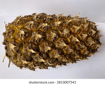 This image shows a close-up of a pineapple’s rough, textured skin. The surface is covered with overlapping hexagonal patterns in shades of brown, yellow, and green, with dry, spiky edges that highlight the fruit’s tough outer layer.