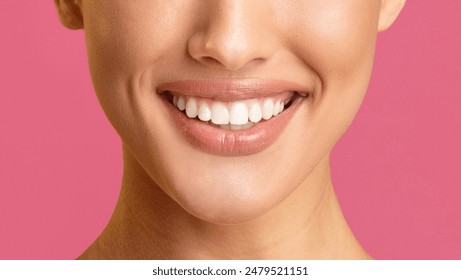 This image shows a close-up view of a womans mouth smiling with her teeth showing. The background is a solid pink color. The focus is on the womans teeth, which are white and straight. - Powered by Shutterstock