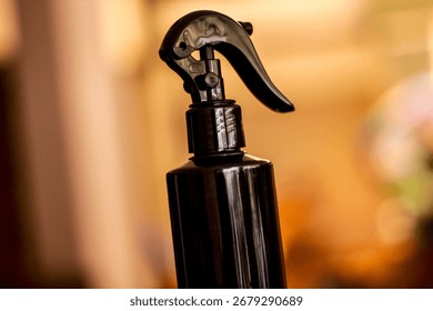 This image shows a close-up view of a dark-colored spray bottle with a sleek and modern design. The bottle features a curved trigger spray nozzle, commonly used for hair care products, cleaning soluti